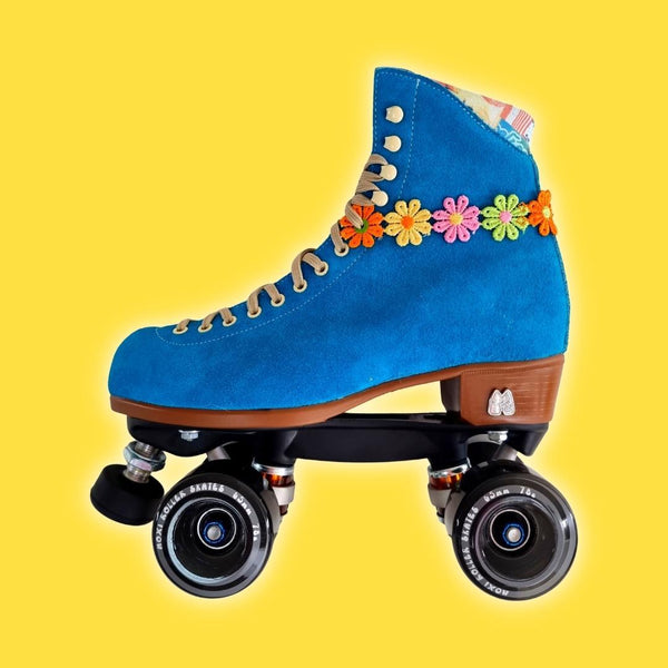 Rollerskate Daisy Chains - Skate Pink Roller Skate Accessories picture of Blue Moxi Lolly with Black Gummy Wheels and toestop with bright coloured daisy chain on bold yellow background.